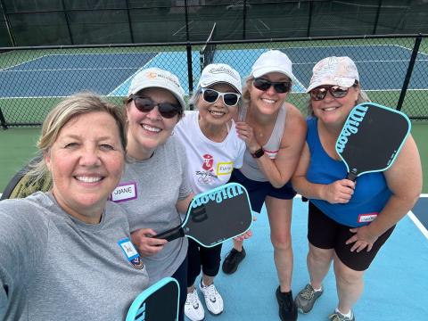Five smiling women on a pickleball court