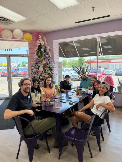 Photo of community members sitting at a table and posing for a photo. 