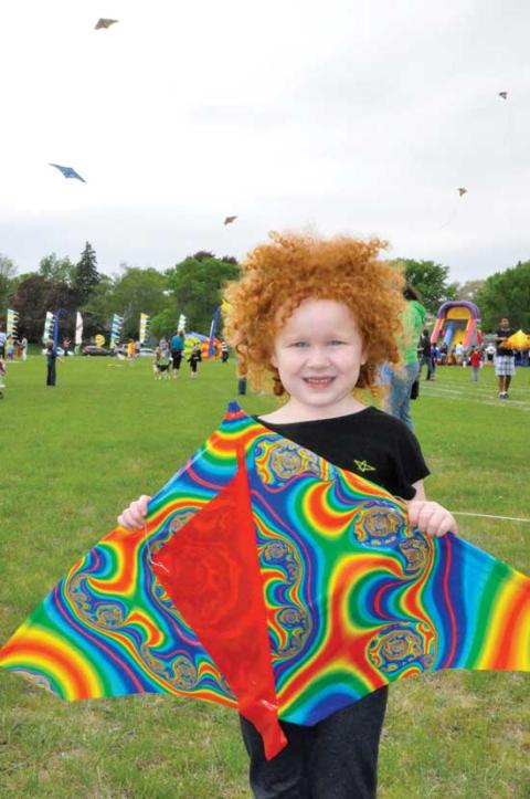 Smiling child holds a colorful kite with many kites in the air in the background