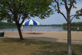 Bush Lake Beach with trees, swimmers, kayaks, and a large umbrella