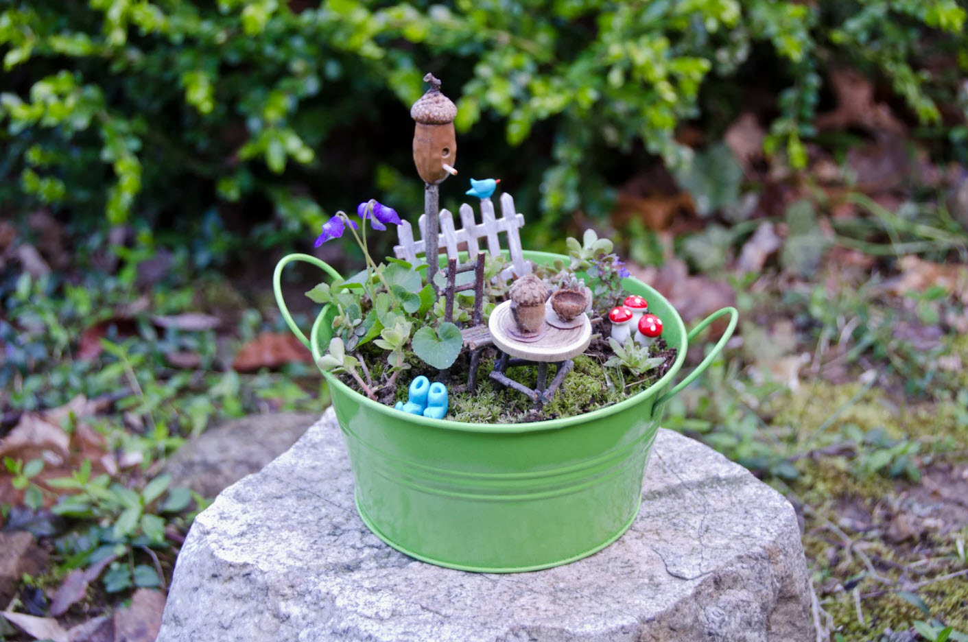 Outdoor scene with small green bucket on a rock with decorative fairy items
