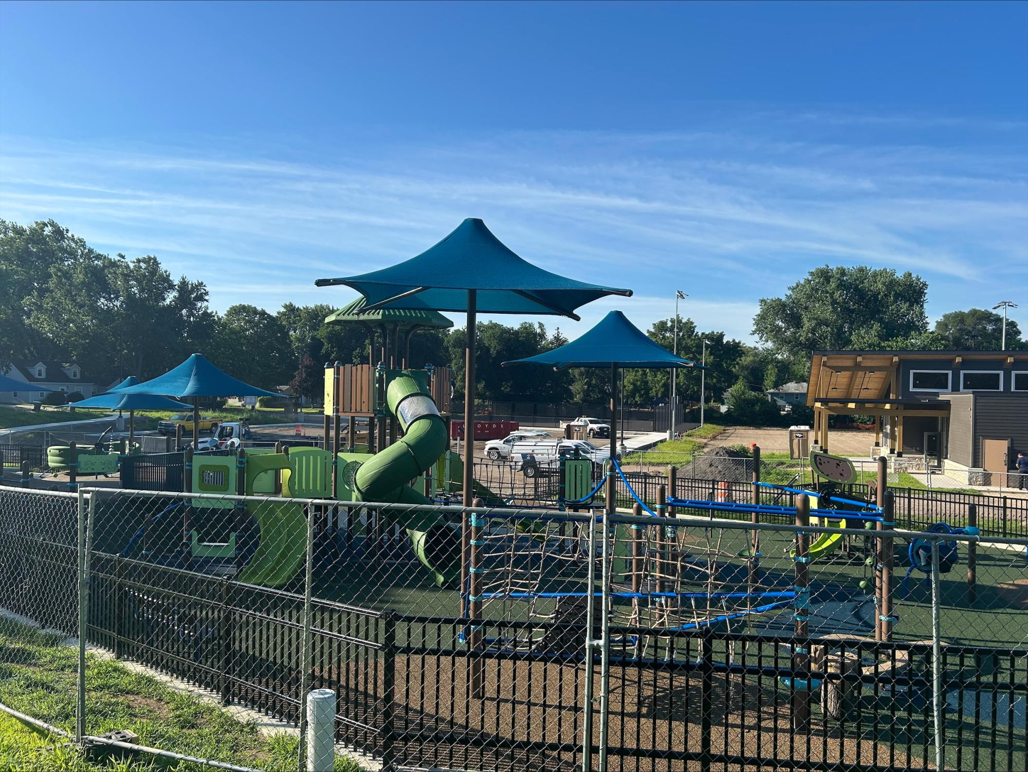 Bryant Park Construction July 8 2025: View of new inclusive playground with brightly colored blue and green apparatus including slides and shade covers