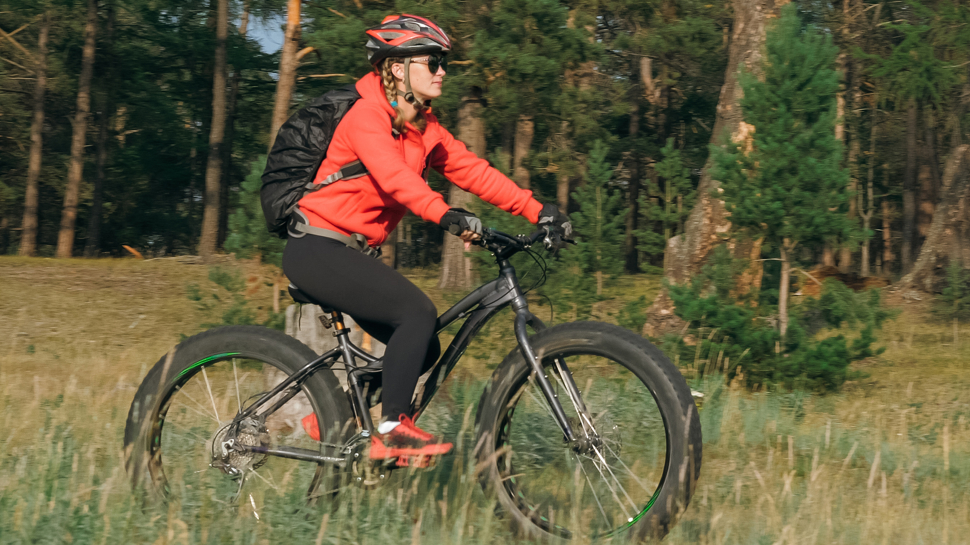 Young woman in red jacket and black pants riding a fat tire bike on a nature trail