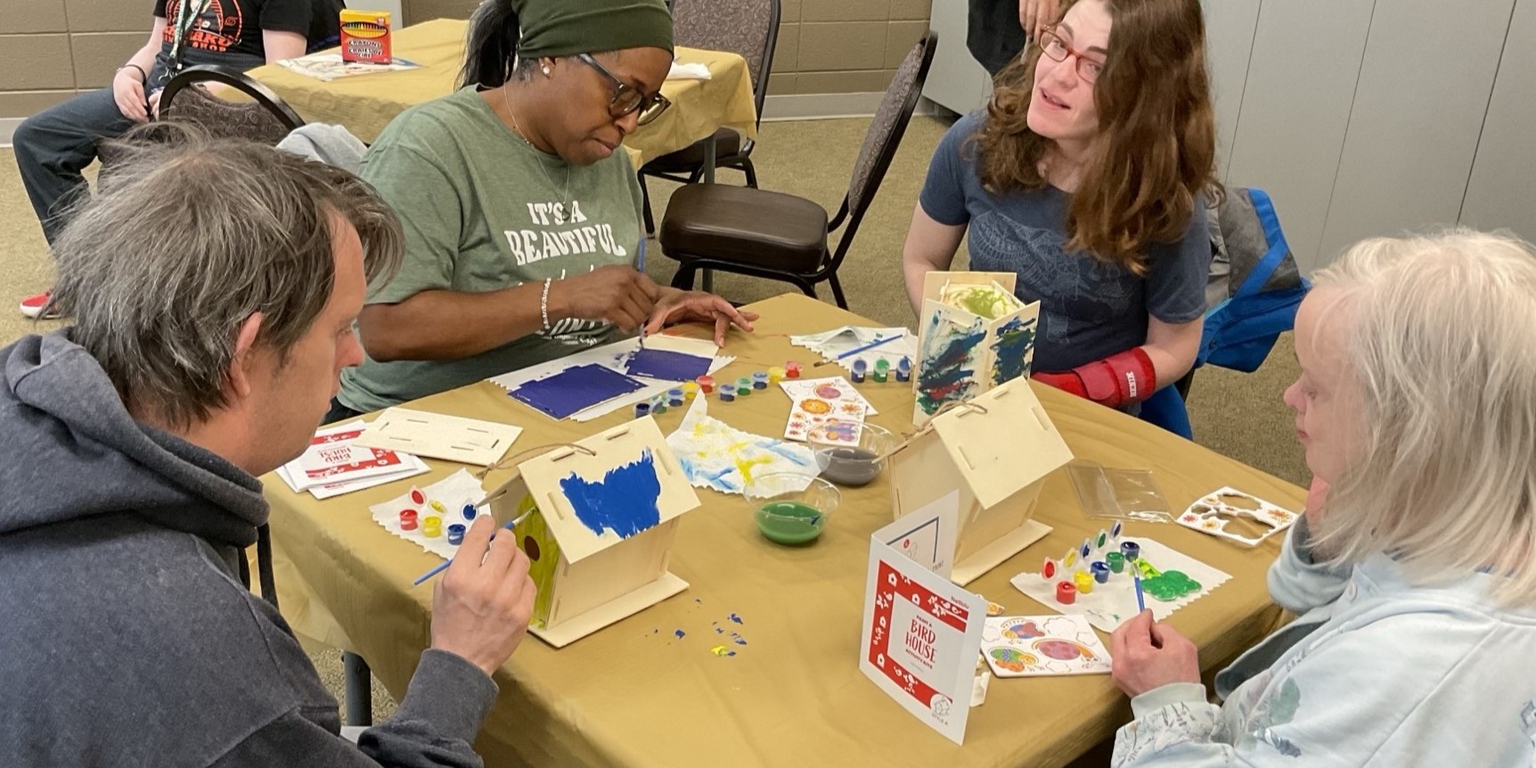 four people at a table painting birdhouses during an adaptive crafts activity