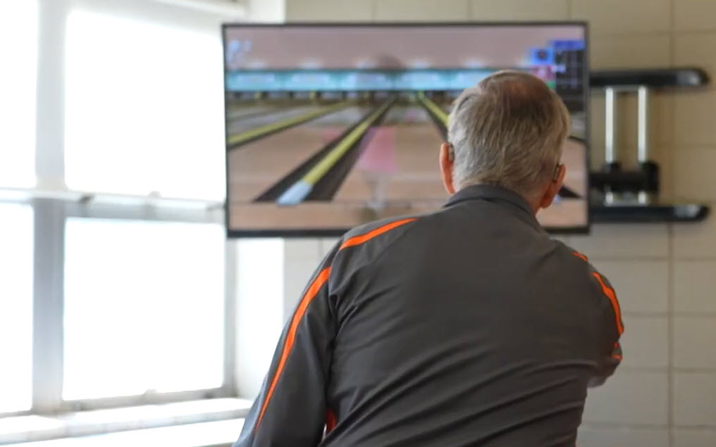 Looking at a man from behind as he plays bowling videogame on a Nintendo Wii