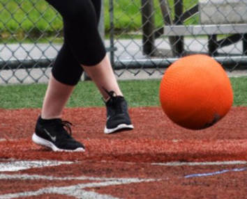 closeup of adult foot kicking a ball during a game of kickball on a baseball diamond