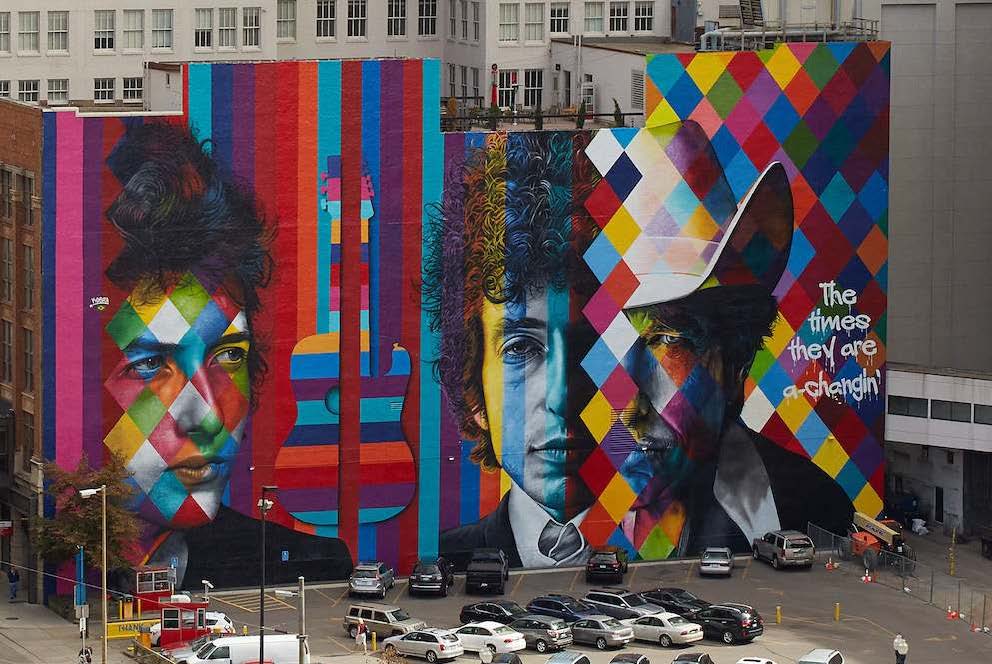 Mural by Eduardo Kobra, colorful wall with stripes, diamonds, and black and white portraits in urban setting