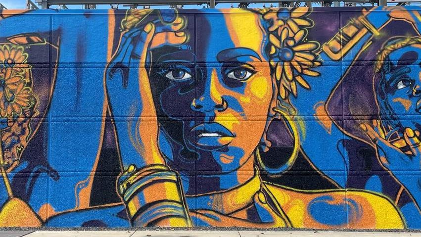 We Mural section by Reggie LeFlore, blue and yellow portraits of three women with arms raised