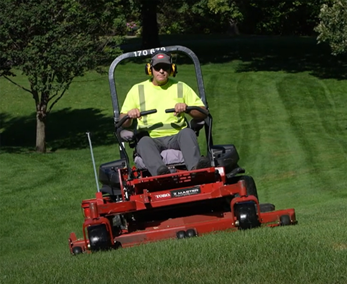 City Park Maintenance staff on a red riding mower mowing grass in a park