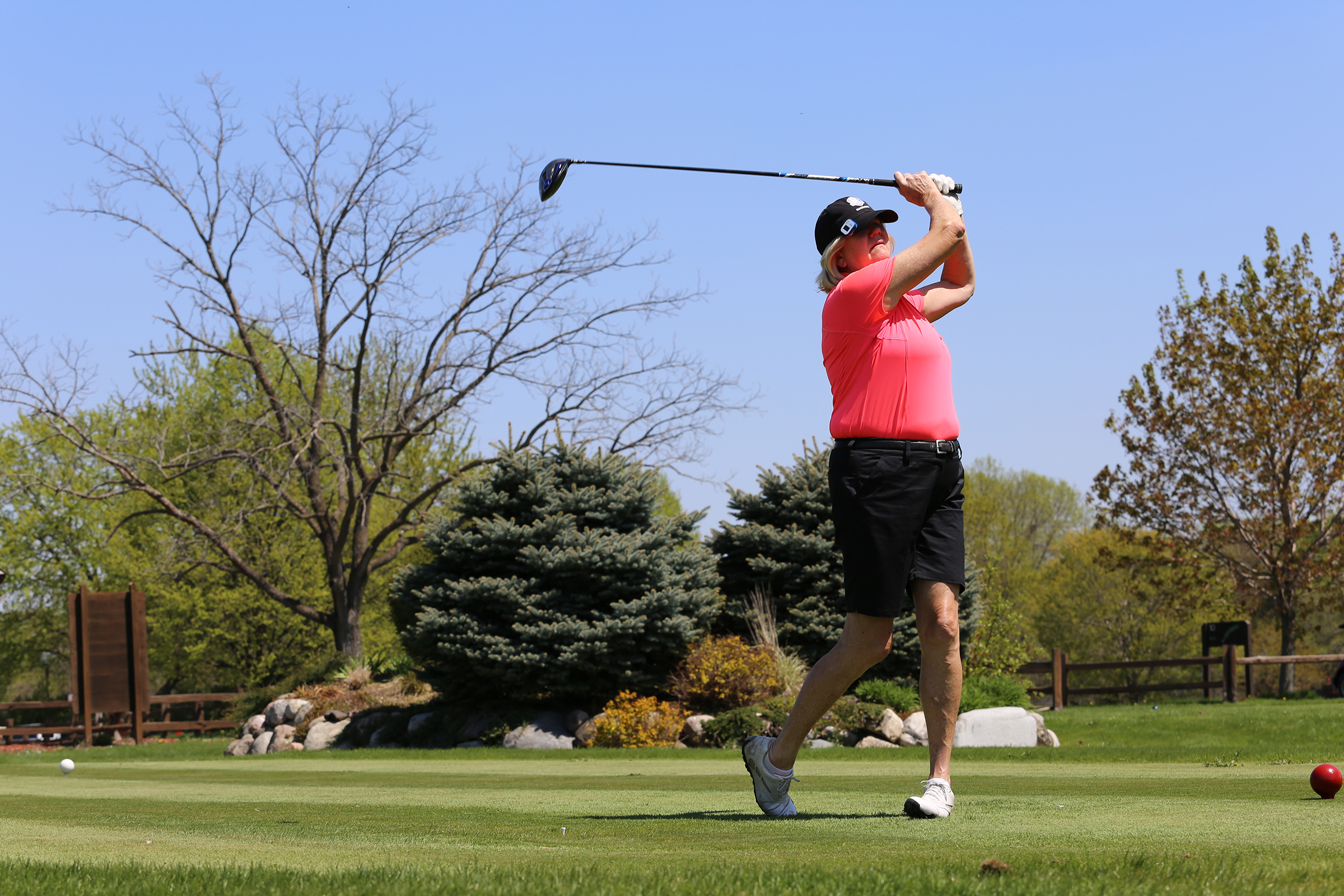 Woman in black hat, red shirt and black shorts teeing off at Dwan Golf Course