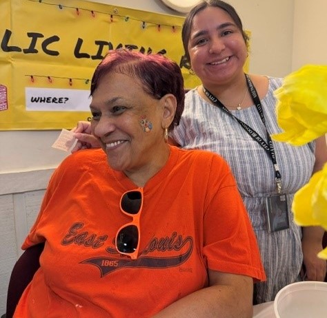Two people smiling with yellow poster in the background 