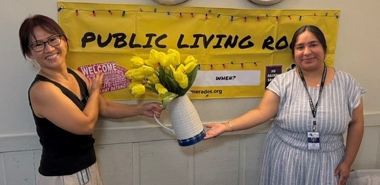 Public Living Space Yellow Poster in the back, two city staff posing with a flower pot