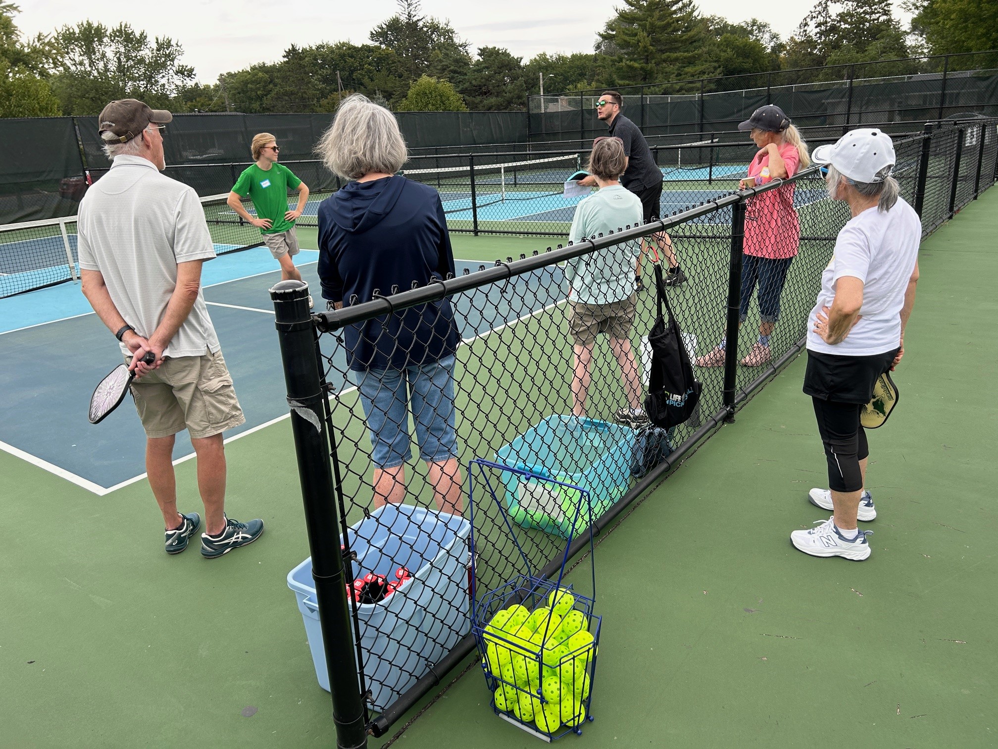 Adults getting a pickleball lesson on an outdoor court