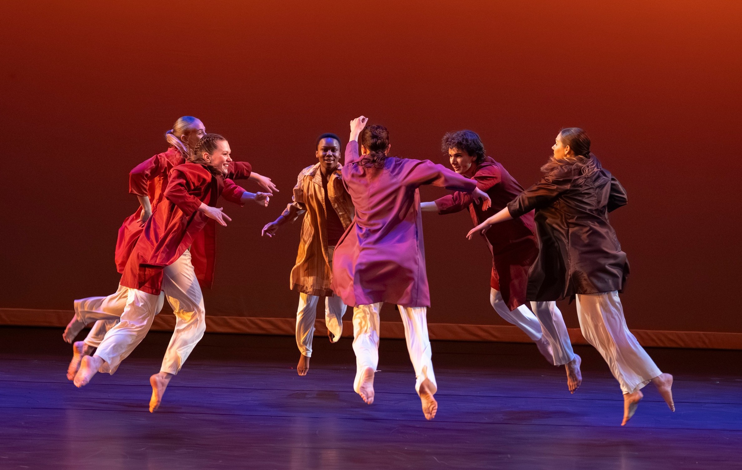 Dancers converging in the center of a stage with a red background