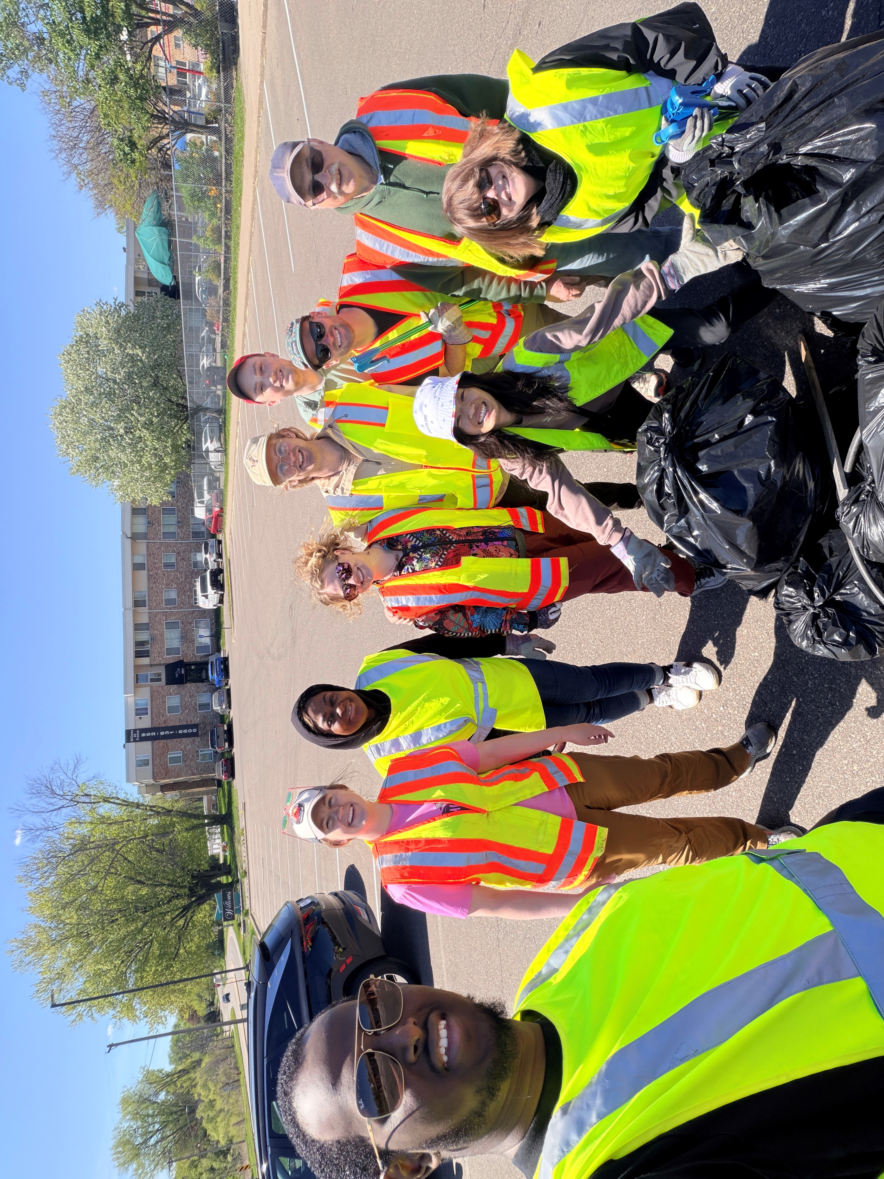 A group of individuals in reflective safety vests smile at the camera with large trash bags in front of them.