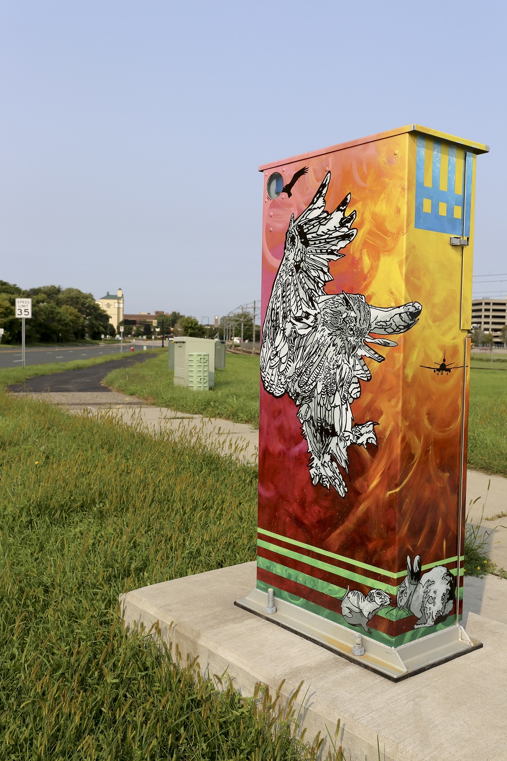 A utility box decorated with a bird flying over a fiery backgound.