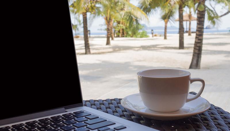 Laptop and coffee cup with tropical beach background