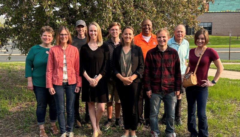 Ten people standing in front of a green tree smiling for a posed photo.