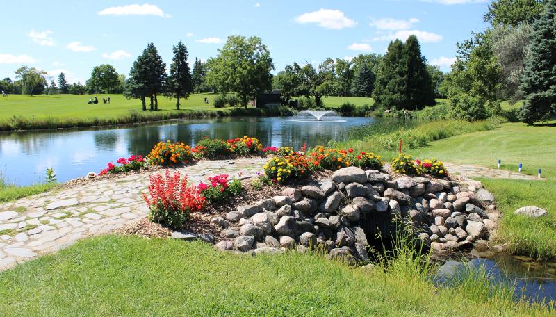 Dwan Golf Course pond with fountain and cobblestone bridge with flowers at Hole 17