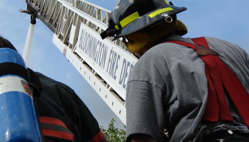 A fireman looking up at a ladder extending up from a truck. 