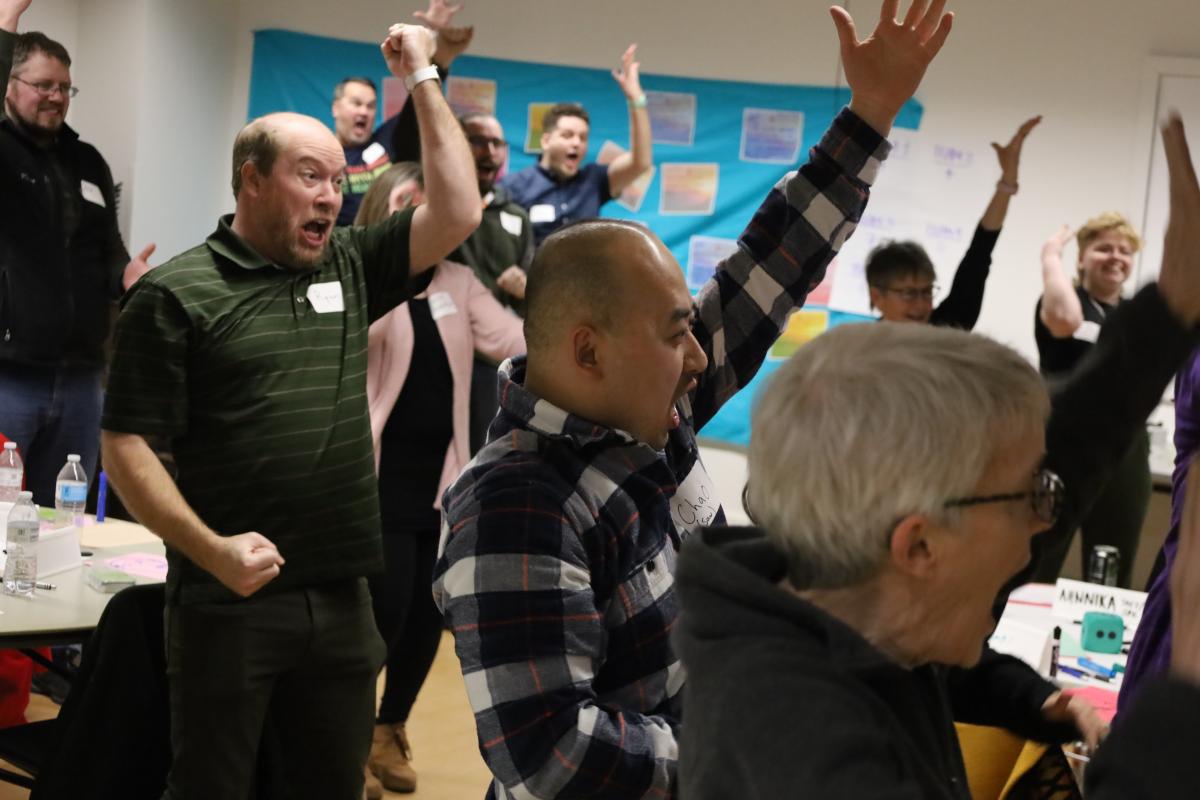 Bloomington Leadership Program alumni, some with hands raised in excitement, stand in a room, appearing to cheer or celebrate.