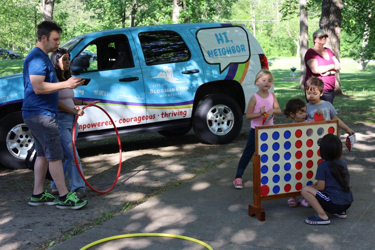 Adults and children are playing with yard gams in front of the Bloomington Engagement Vehicle.