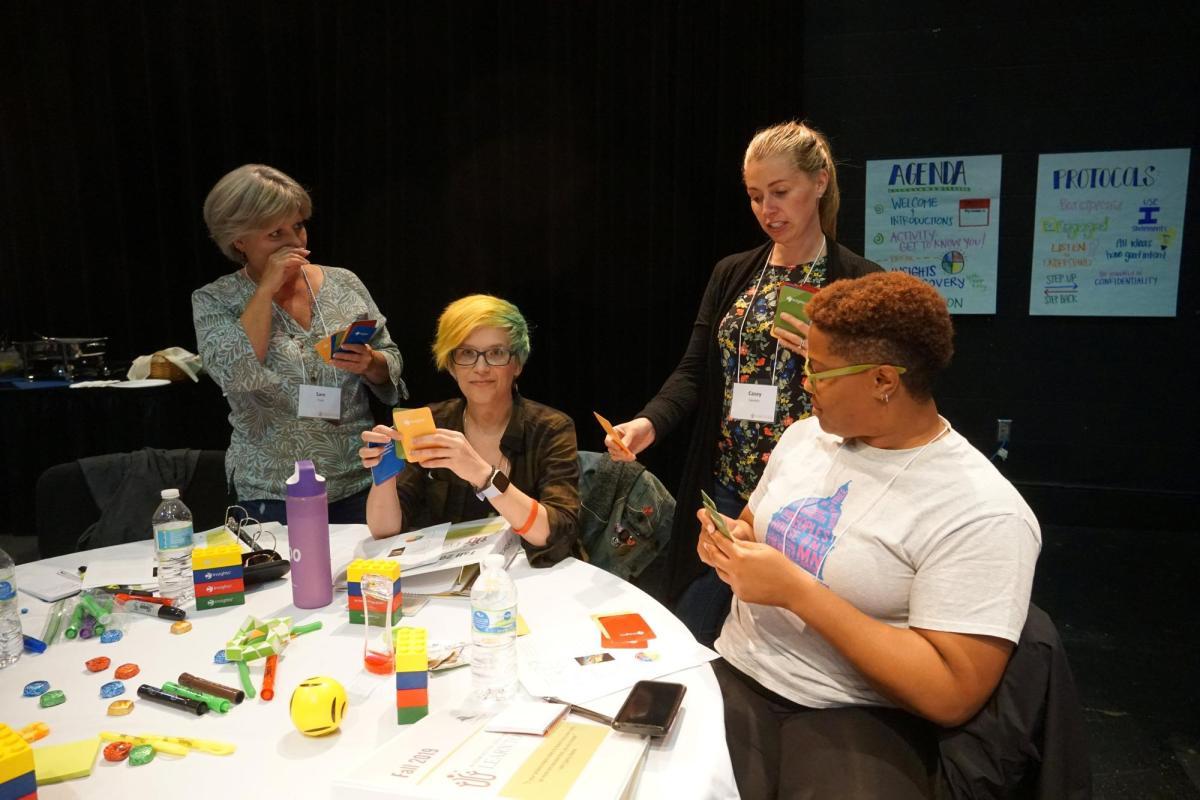 Four adults gather around a table during session, interacting with colorful cards and building blocks