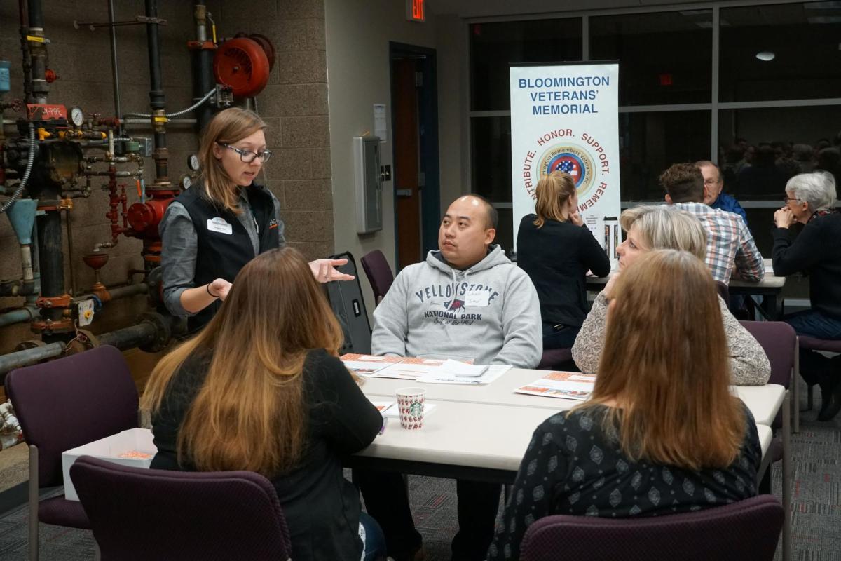 A group of four adults listen to another adult presenting to the table