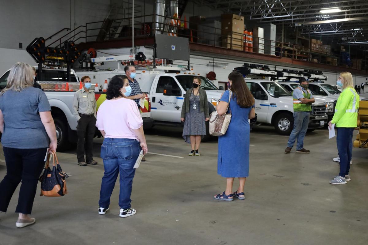 A group of adults gather in the Public Works garage with City of Bloomington vehicles in the background