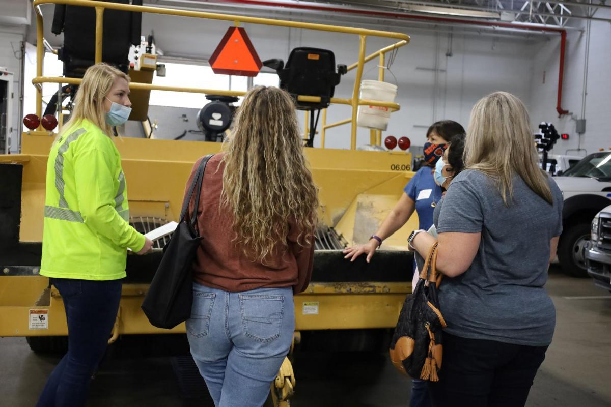 A group of adults stand in front of public works machinery 