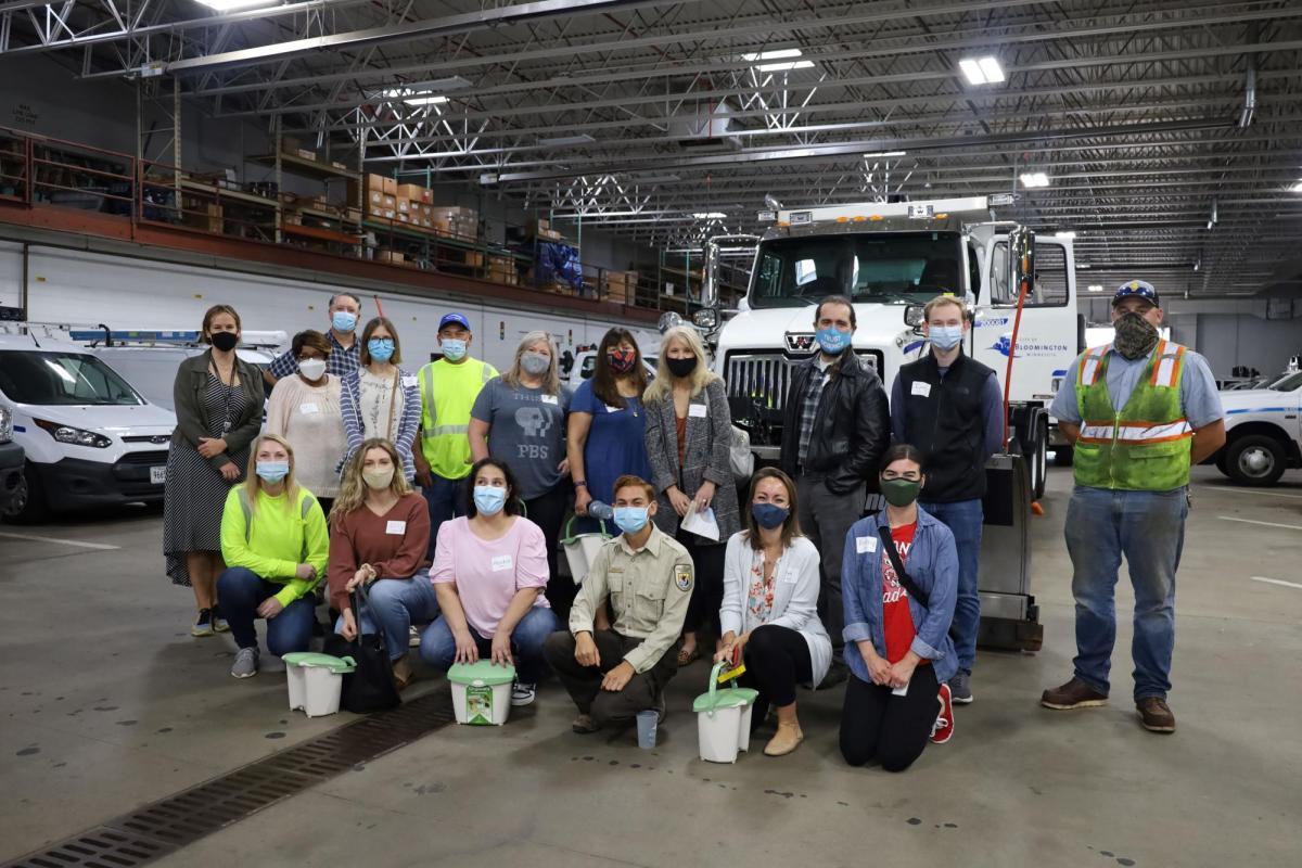 The participants are in the public works garage, smiling at the camera