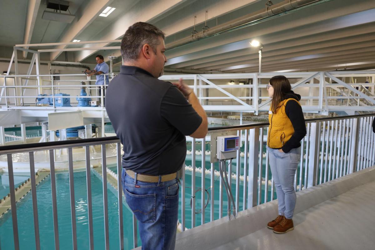 Two individuals stand near a railing, above the water in a water treatment plant