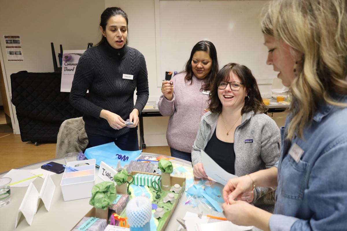 Four people gathered around a table, collaborating on a miniature landscape
