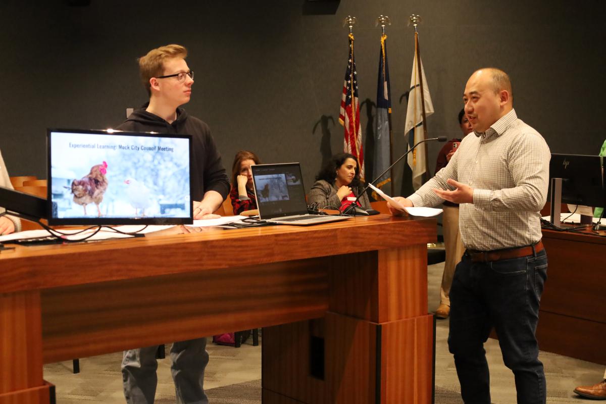 A particpant stands at the Council Chamber podium with a councilmember