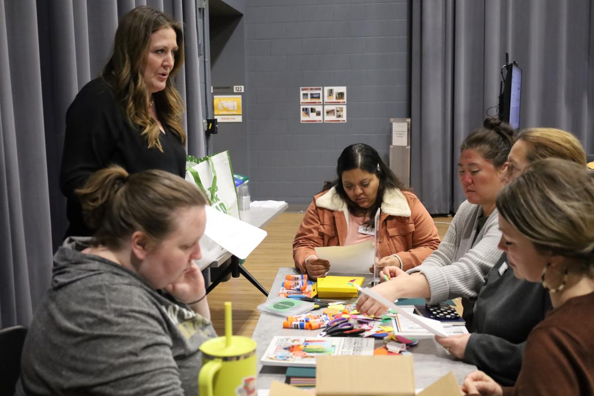 People working on a collaborative craft project at a table, supervised by another individual