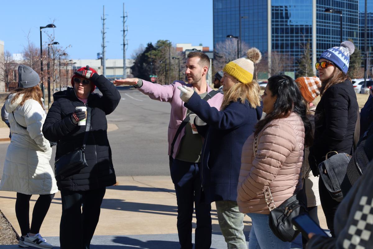 A group of people standing outside while two point in the same direction