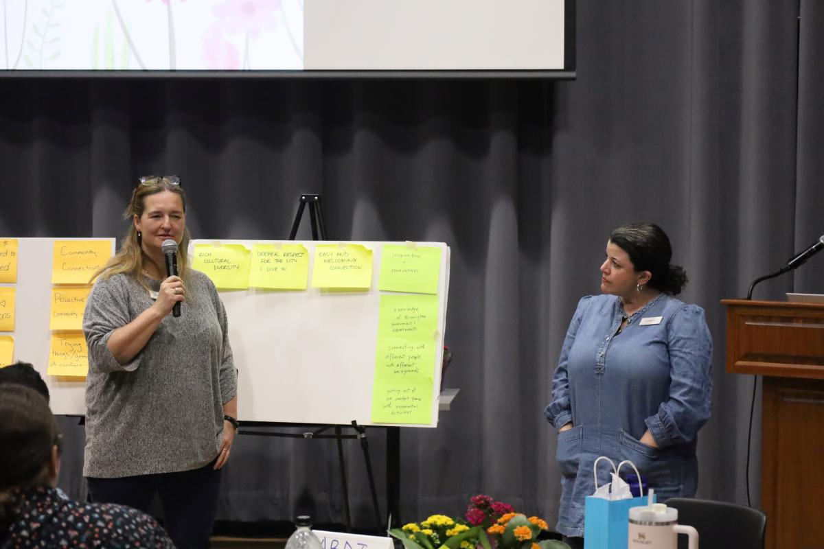 Two people stand and present in front of poster boards with large sticky notes
