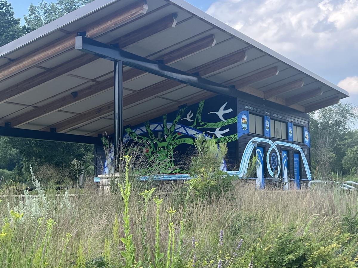 Trailhead building with murals, roofed picnic shelter, native plants in foreground
