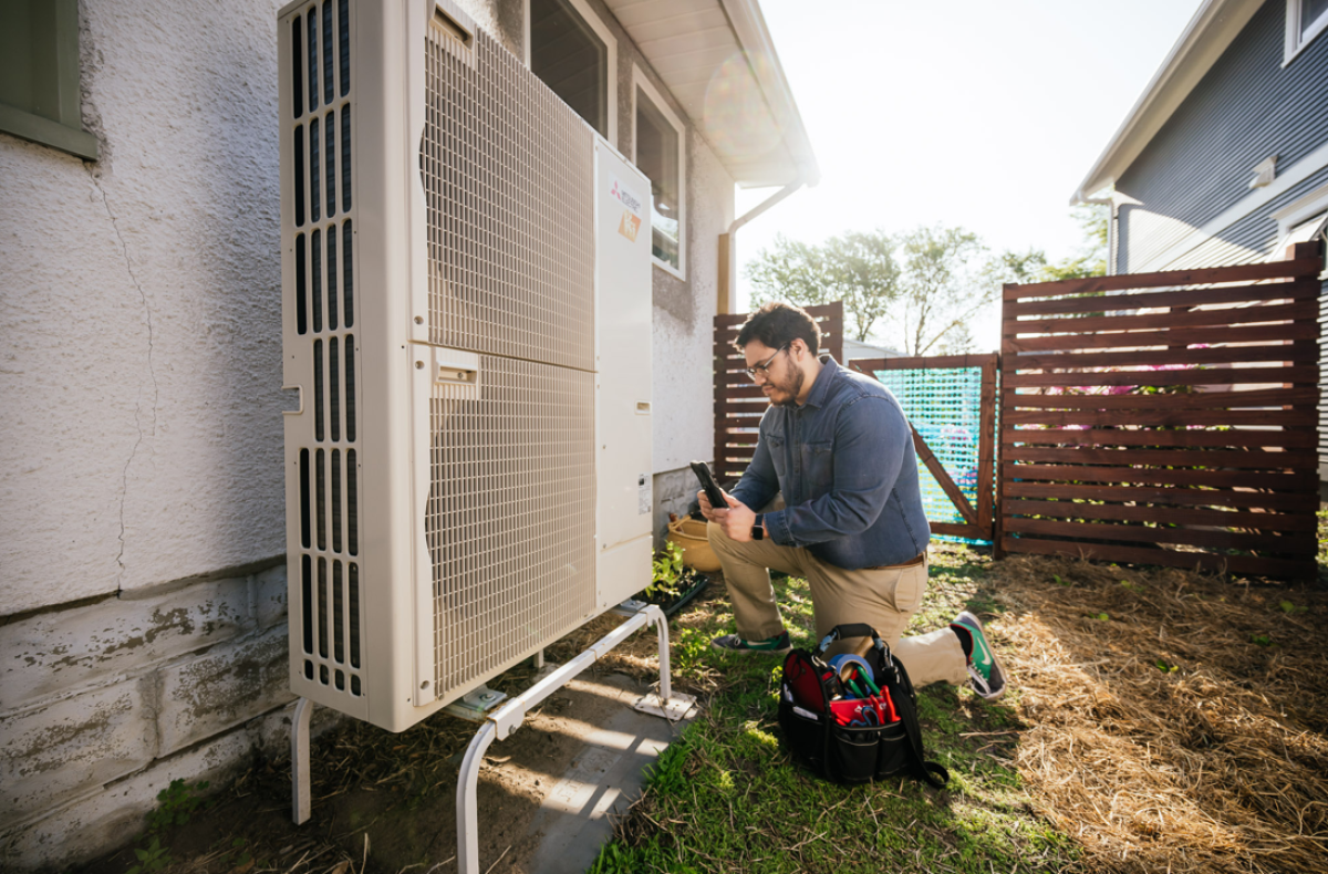 Person kneeling next to heat pump condenser