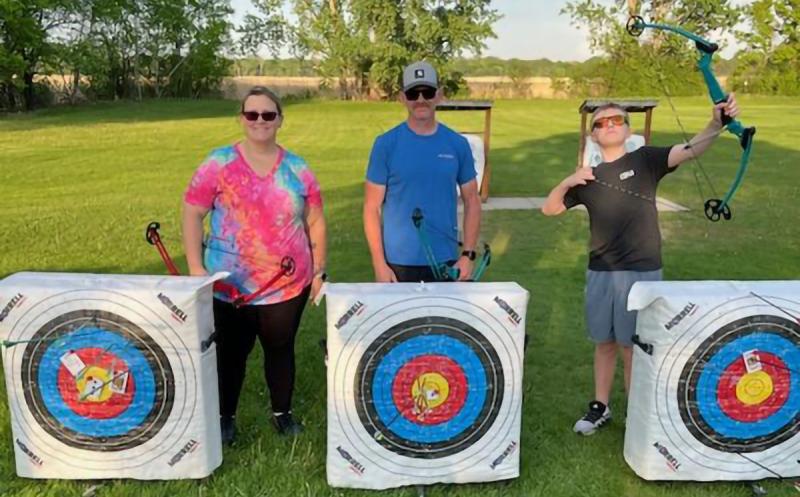 Family at archery range standing near targets holding compound bows