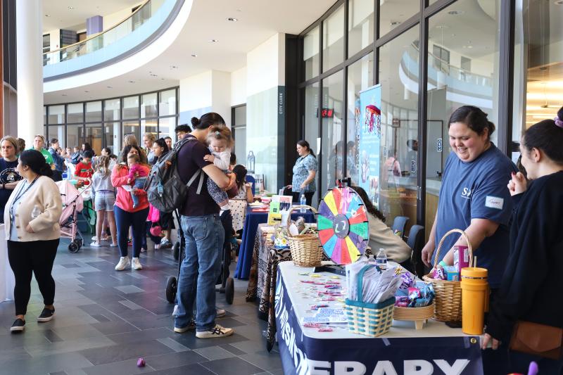 People holding young children browse exhibitor tables at the Early Childhood Expo 