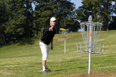 Man in hat throwing disk towards basket on Disc Golf course