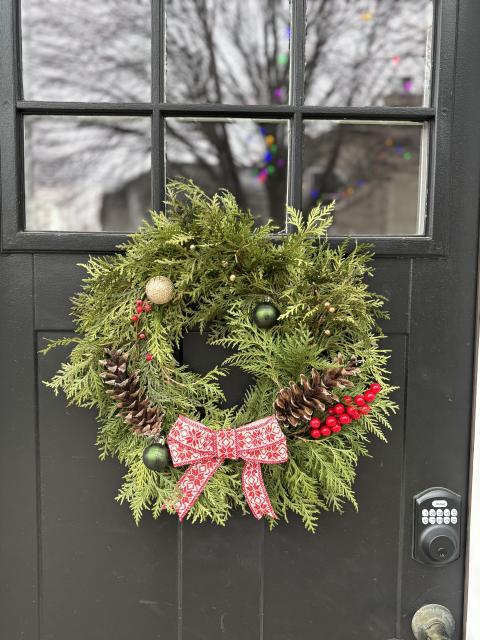 Green wreath with red ribbon and berries hanging on a black door in winter