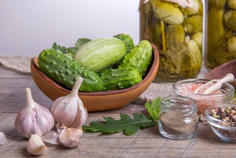 Bright green pickles in a bowl on a table with garlic and other ingredients