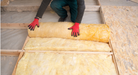 A kneeling person wearing red gloves rolls out yellow insulation