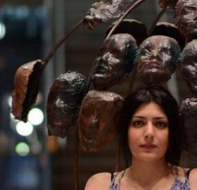 Woman with dark hair in lower right corner standing in front of sculpture of faces