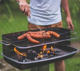 A person grilling hotdogs outdoors